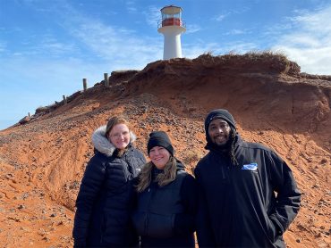 Photo de deux étudiantes et un étudiants en technique d'éducation à l'enfance, devant un phare aux iles de la madeleine, pendant leur stage de fin d'études