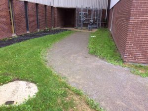 L'environnement de la porte 9 avant les travaux. Une allée de poussière de roche bordée de gazon.